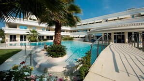 A pool area with a palm tree, a building with multiple balconies, and a covered walkway. - 103 Relais du Lac Village - Italian Homing (Desenzano del Garda)