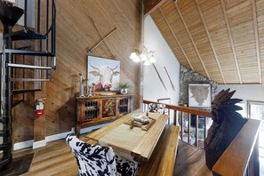 A wooden interior with a dining table, chairs, a fireplace, and a staircase.
