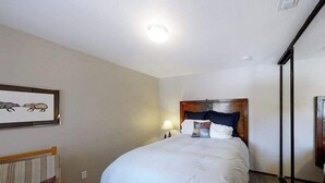 A hotel room with a bed, a nightstand, a lamp, a framed picture on the wall, and a window. - Top Deck Retreat - Huntington Lake (Lakeshore)