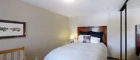 Et hotelværelse med seng, et natbord, en lampe, et billede i ramme på væggen og et vindue.
