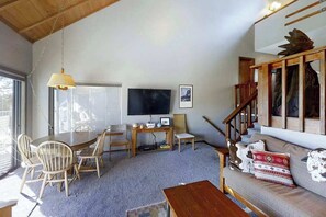 Un salon chaleureux avec une table à manger en bois, des chaises, un canapé, un téléviseur et un escalier.
