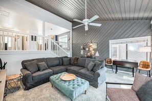 A modern living room with a sectional sofa, a round ottoman, a ceiling fan, and a staircase leading to an upper level.