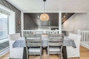 A dining area with a table and chairs, a hanging light fixture, and a view of the outdoors.