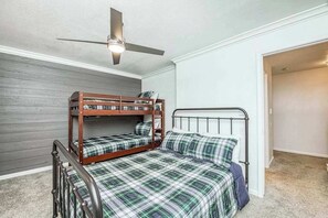 A room with two bunk beds, a ceiling fan, and a door leading to another room.