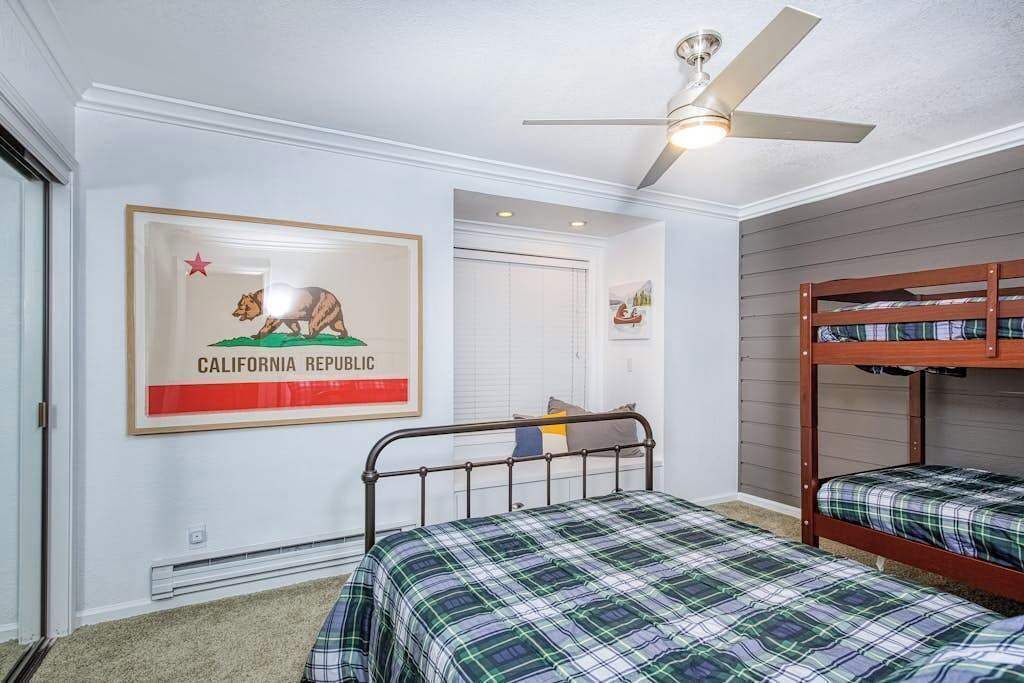 Une chambre avec deux lits superposés, un ventilateur de plafond et une affiche de la Californie sur le mur.