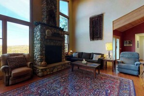 A spacious living room with a stone fireplace, a large window, a patterned rug, and a blue armchair. - Pine Mountain Getaway - Pine Mountain Lake (Groveland)