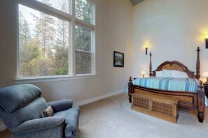 A bedroom with a large window, a bed with a wooden headboard, a blue armchair, and two wall-mounted lamps. - Pine Mountain Getaway - Pine Mountain Lake (Groveland)