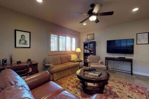 A living room with a sofa, a coffee table, a television, a bookshelf, and a ceiling fan.