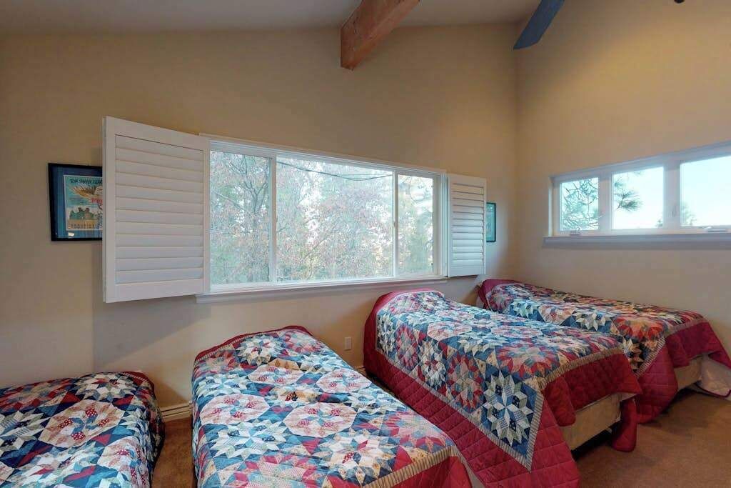 Un dormitorio con dos camas, un ventanal con contraventanas y un cuadro en la pared.