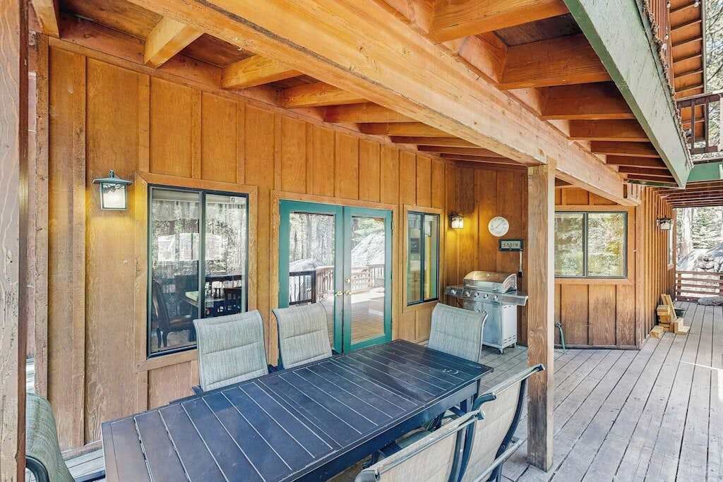 Un terrazzo in legno con tavolo e sedie, un barbecue e vista sull'esterno.