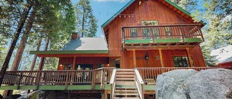 A wooden cabin with a balcony, surrounded by trees.