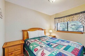 A bedroom with a wooden bed, a nightstand, a lamp, and a window with curtains. - The Rockin' Buffalo - Granite Ridge (Shaver Lake)
