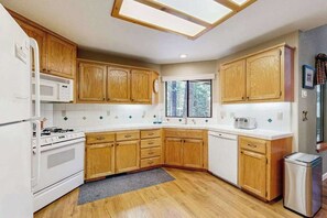A kitchen with wooden cabinets, a white stove, a microwave, and a window. - The Rockin' Buffalo - Granite Ridge (Shaver Lake)