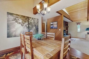 A dining area with a wooden table and chairs, a chandelier, and a large painting on the wall. - Whispering Pines - Sierra Cedars (Shaver Lake)