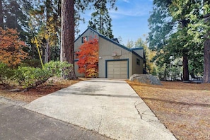 A two-story building with a garage door, surrounded by trees and a driveway. - Whispering Pines - Sierra Cedars (Shaver Lake)