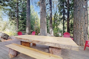 A wooden deck with a picnic table and red chairs, surrounded by tall trees. - Whispering Pines - Sierra Cedars (Shaver Lake)