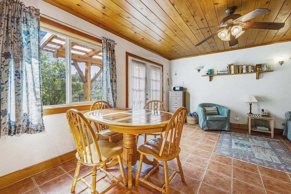 A dining area with a wooden table and chairs, a ceiling fan, and a view through a window.