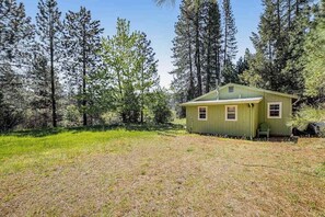A small, single-story cabin with a green exterior, surrounded by a forested area. - Yosemite Mountain Cottage - Groveland (Groveland)