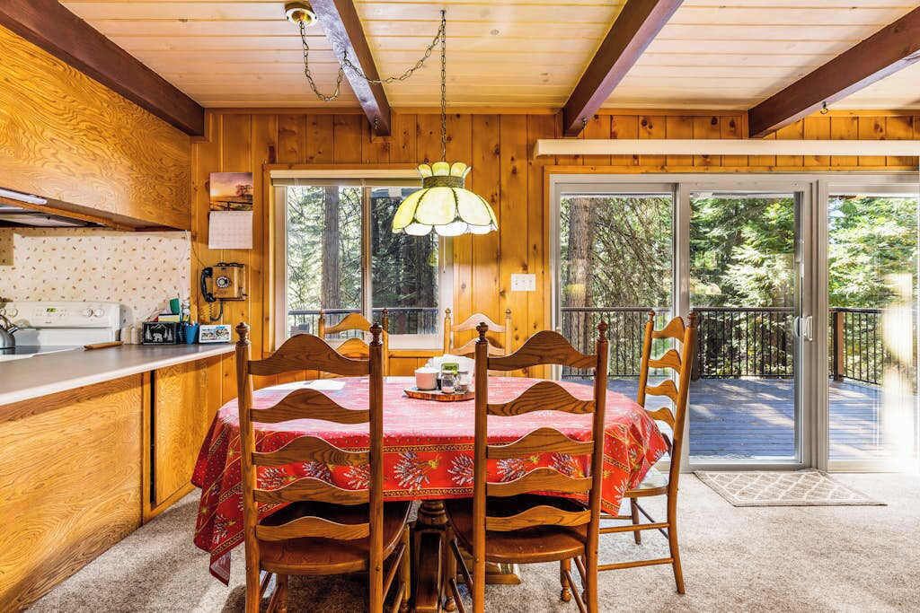 A wooden interior with a dining table and chairs, a kitchen area, and a sliding glass door leading to an outdoor deck.