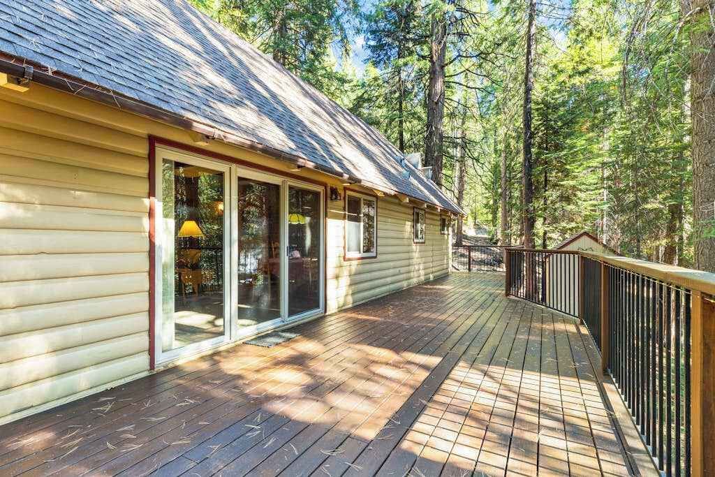 A wooden deck with a railing, a building with a sloped roof, and a forested background.