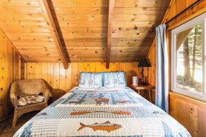 Ein Zimmer einer Holzhütte mit einem Bett, einem Sessel und einem Fenster.