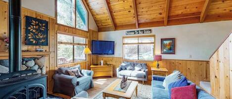 A cabin interior with a wooden ceiling, a fireplace, and two sofas.