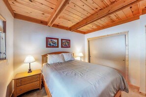 A bedroom with a wooden ceiling, a bed with white bedding, two bedside lamps, and two framed pictures on the wall. - Pine Paradise - Big Trees Villag (Camp Connell)