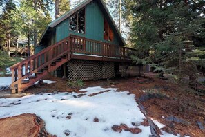 A cabin with a wooden staircase leading to a deck, surrounded by trees and snow. - Pine Paradise - Big Trees Villag (Camp Connell)