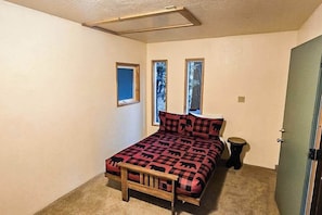 Une chambre à coucher avec un lit, une fenêtre, une porte et un petit tabouret.