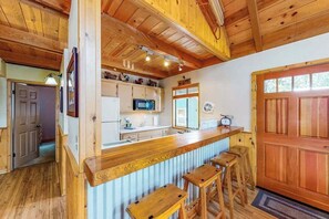 A kitchen with wooden cabinets, a microwave, and a bar area with stools. - Pine Paradise - Big Trees Villag (Camp Connell)