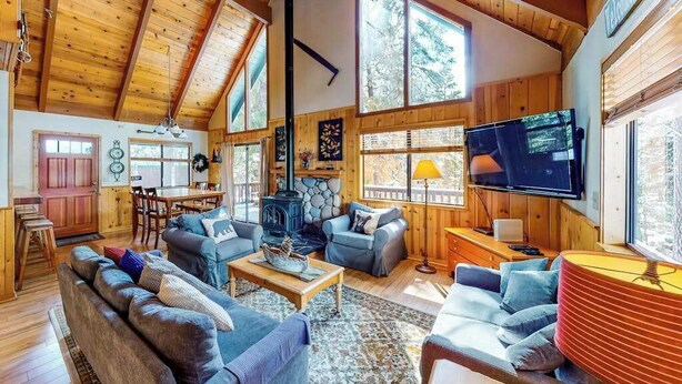 Ein geräumiges Wohnzimmer mit hoher Decke, Holzwänden, Kamin, Fernseher und Essbereich.