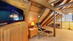 Ein Zimmer mit Holzboden, einem Fernseher, einem Schreibtisch mit Lampe, einem Stuhl und einem kleinen Tisch.