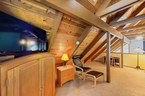 Ein Zimmer mit Holzboden, einem Fernseher, einem Schreibtisch mit Lampe, einem Stuhl und einem kleinen Tisch.