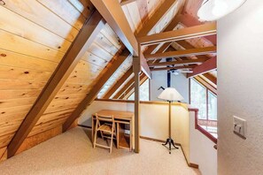 A room with sloped wooden ceilings, a small desk, a chair, and a floor lamp. - Pine Paradise - Big Trees Villag (Camp Connell)