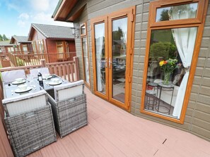 A covered outdoor patio with wicker furniture and a dining table set for four. - 10 Poppy Lodge (Richmond)