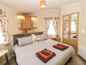 A bedroom with a bed, a bedside table, a mirror, a wardrobe, and a shelf with decorative items. - 10 Poppy Lodge (Richmond)
