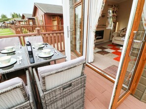A patio with a table set for dining, wicker chairs, and a view of wooden cabins in the background. - 10 Poppy Lodge (Richmond)