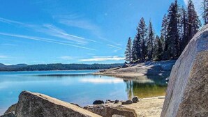 A natural landscape with a calm lake, rocky shore, and dense forest. - Tranquil Pines Estate - Ridgetop (Shaver Lake)