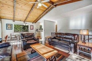 Un vaste espace de vie doté d’un haut plafond, de canapés en cuir, d’une table basse en bois et d’un ventilateur de plafond.