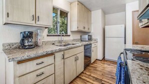 Eine kleine Küche mit Holzschränken, einer Mikrowelle, einer Kaffeemaschine und einem Kühlschrank.