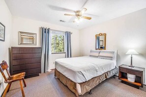 A bedroom with a bed, a chair, a nightstand, a ceiling fan, a window with curtains, and a framed picture on the wall. - Bryant Cabin - Blue Lake Springs (Arnold)