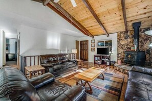 A spacious living room with a high ceiling, a stone fireplace, leather sofas, and a television. - Bryant Cabin - Blue Lake Springs (Arnold)
