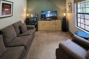 Ein Wohnzimmer mit großem Flachbildfernseher, einer Holzkabine, einer Couch und einem kleinen Tisch.