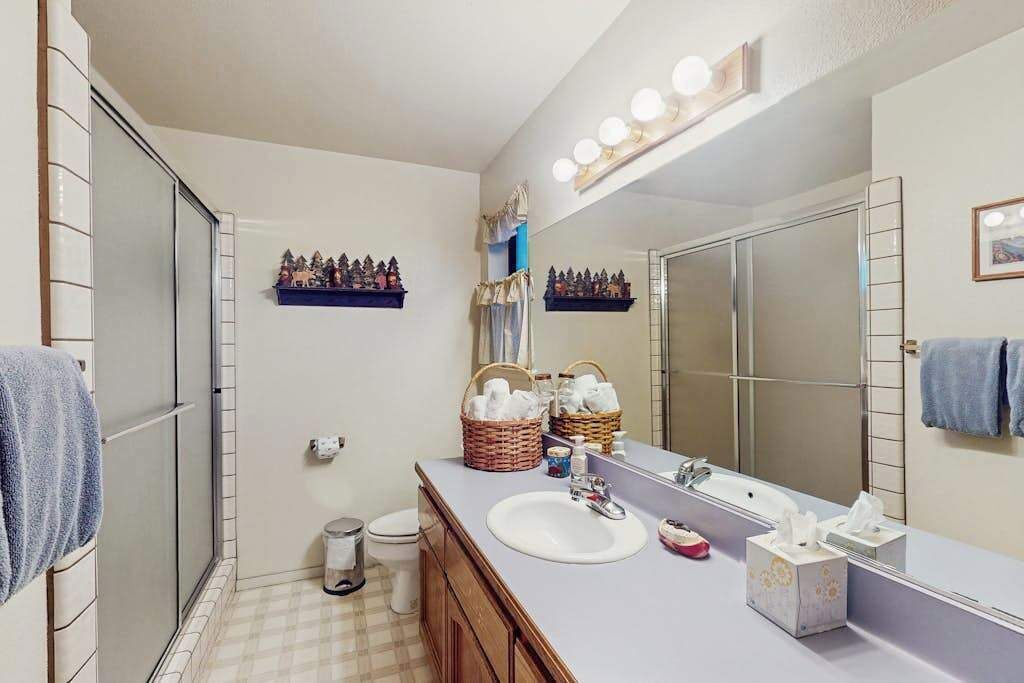 A bathroom with a large mirror, a sink, a toilet, and a shower area. There are decorative items on the wall and a towel rack.