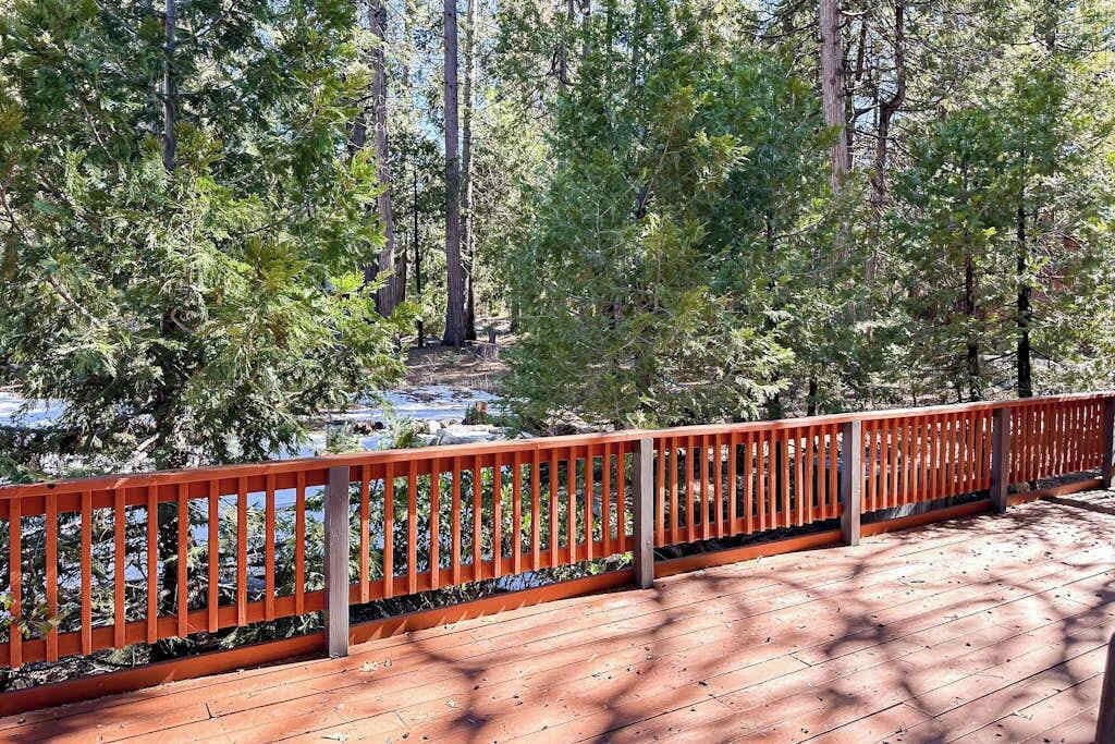 A wooden deck with a red railing overlooking a forested area with a stream.