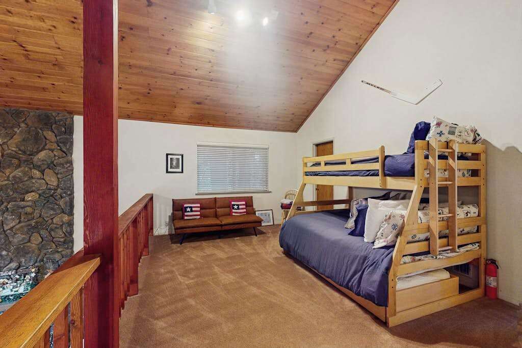 Une pièce avec un lit superposé, un canapé, un mur en pierre et un plafond en bois.