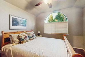 Un dormitorio con cama, ventilador de techo, ventana con persianas e imagen enmarcada en la pared.