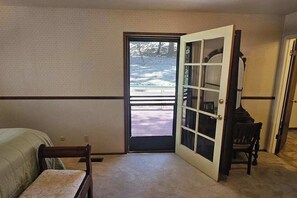 Ein Zimmer mit Bett, einem Sessel, einer zur Außenwelt hin führenden Tür und Blick auf eine verschneite Landschaft.