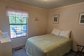 A bedroom with a bed, a window with a view of outdoor furniture, and a wall-mounted shelf. - Forest Treasure - Pine Mountain Lake (Groveland)