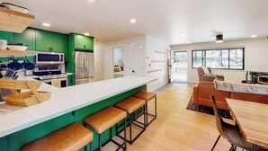 A modern kitchen with green cabinets, a white island, and a dining area with a wooden table and chairs. - Piney Point - Meadowmont (Arnold)